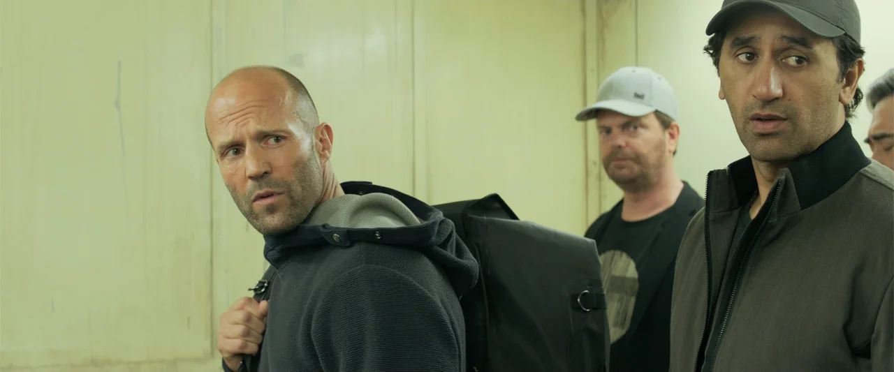 The Meg (2018) movie still: medium — A utilitarian elevator interior features light yellow metal walls and overhead fluorescent lights. Three men…