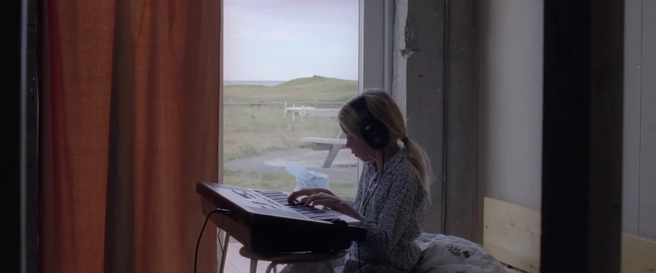 A White, White Day (2019) movie still: medium — A child plays a keyboard in front of a window overlooking a grassy hill. The interior features…