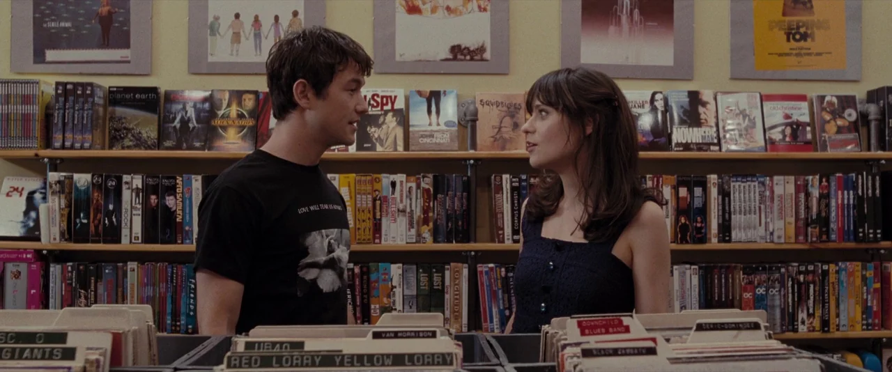 500 Days of Summer (2009) movie still: medium — A media store aisle features wooden shelves stocked with various films and music records. Two young…