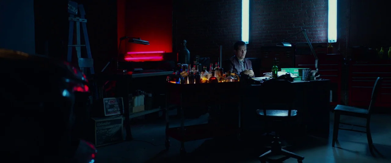 John Wick: Chapter 2 (2017) movie still: wide — A dimly lit industrial workshop features exposed brick walls and scattered automotive tools. A man…
