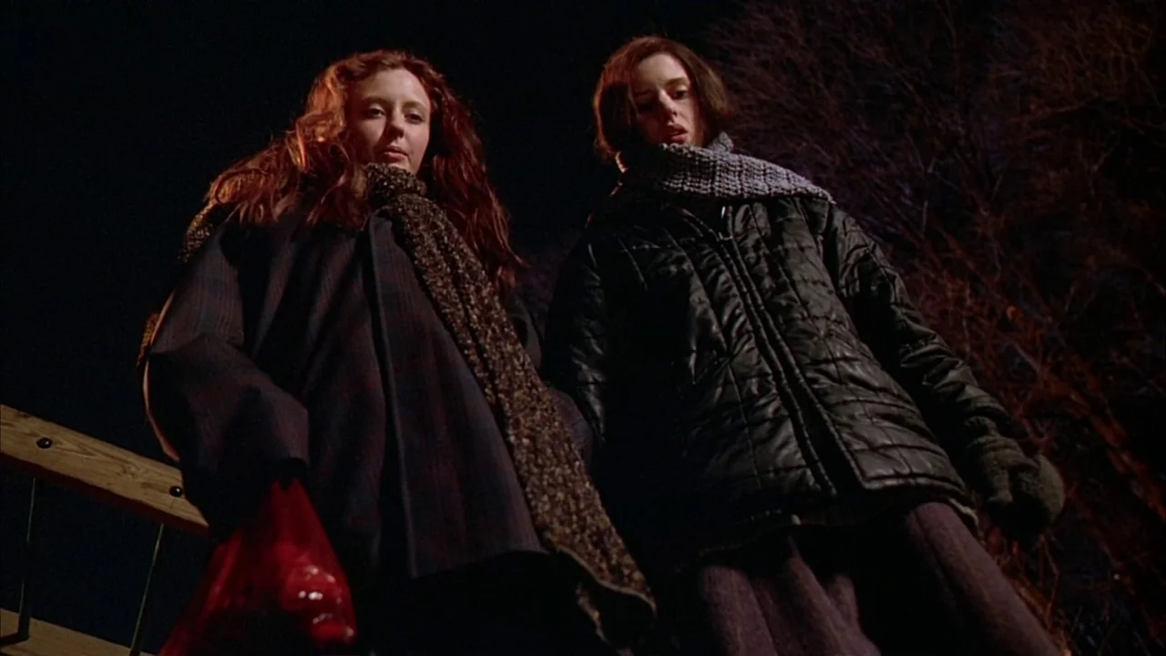 Ginger Snaps (2000) movie still: medium — Two women stand outdoors at night, their faces illuminated from below in the dark. They stare downward…