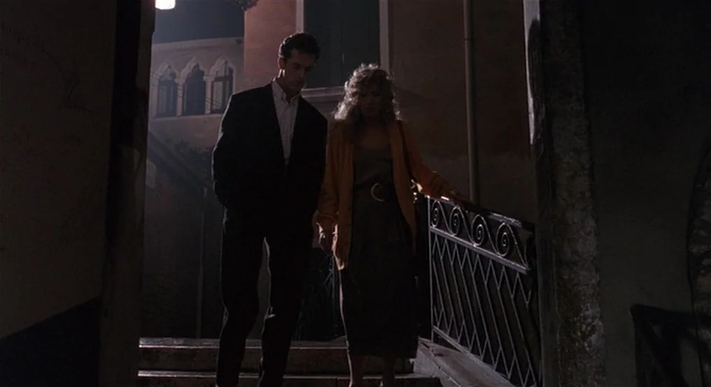 The Comfort of Strangers (1990) movie still: fullbody — A dark outdoor stone staircase leads down between old European buildings at night. A man and…
