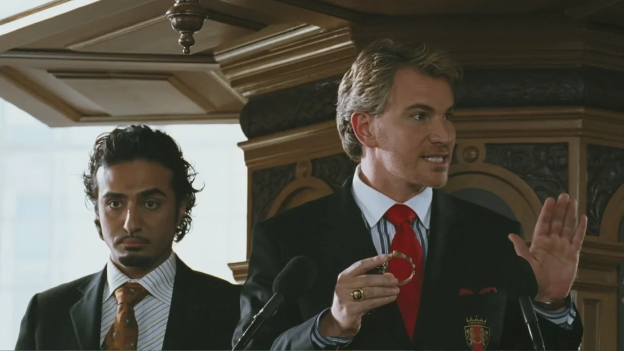 Deuce Bigalow: European Gigolo (2005) movie still: medium — A man in a suit speaks behind a dark wooden podium. A second man stands slightly behind…