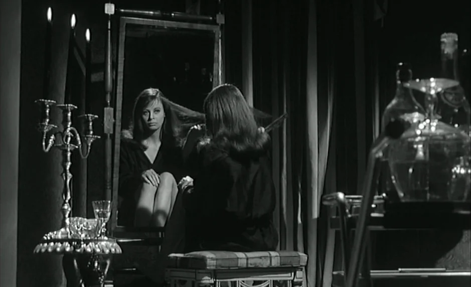 The Servant (1963) movie still: medium — A dimly lit room contains a vanity table with a tall rectangular mirror. A woman sits on a stool brushing…
