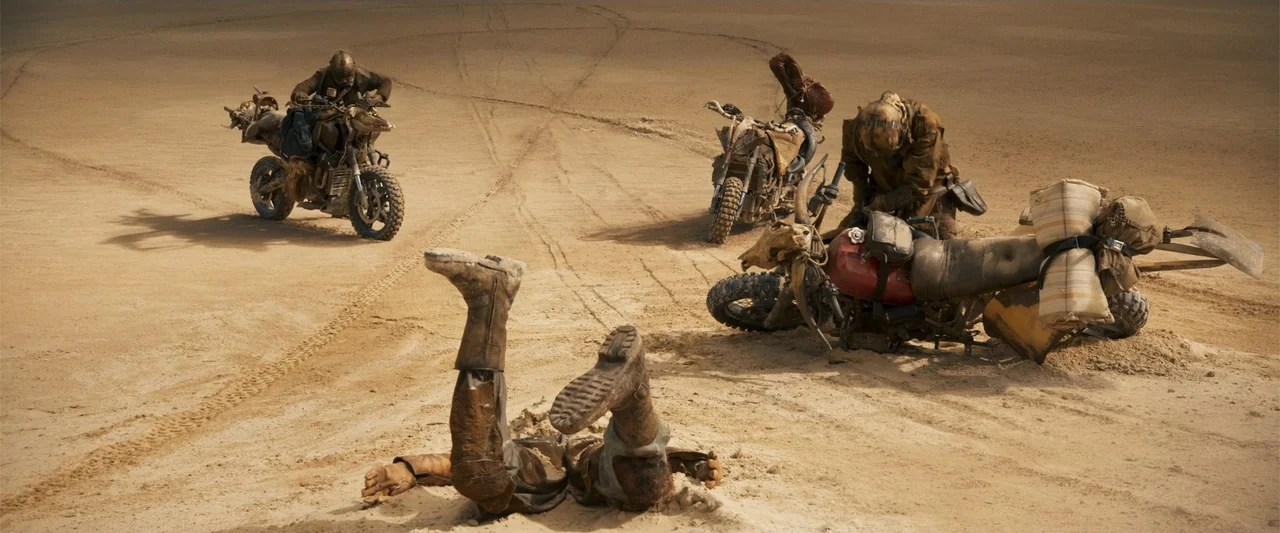 Furiosa: A Mad Max Saga (2024) movie still: wide — A vast expanse of barren desert sand shows tire tracks from multiple motorcycles. Three armored…