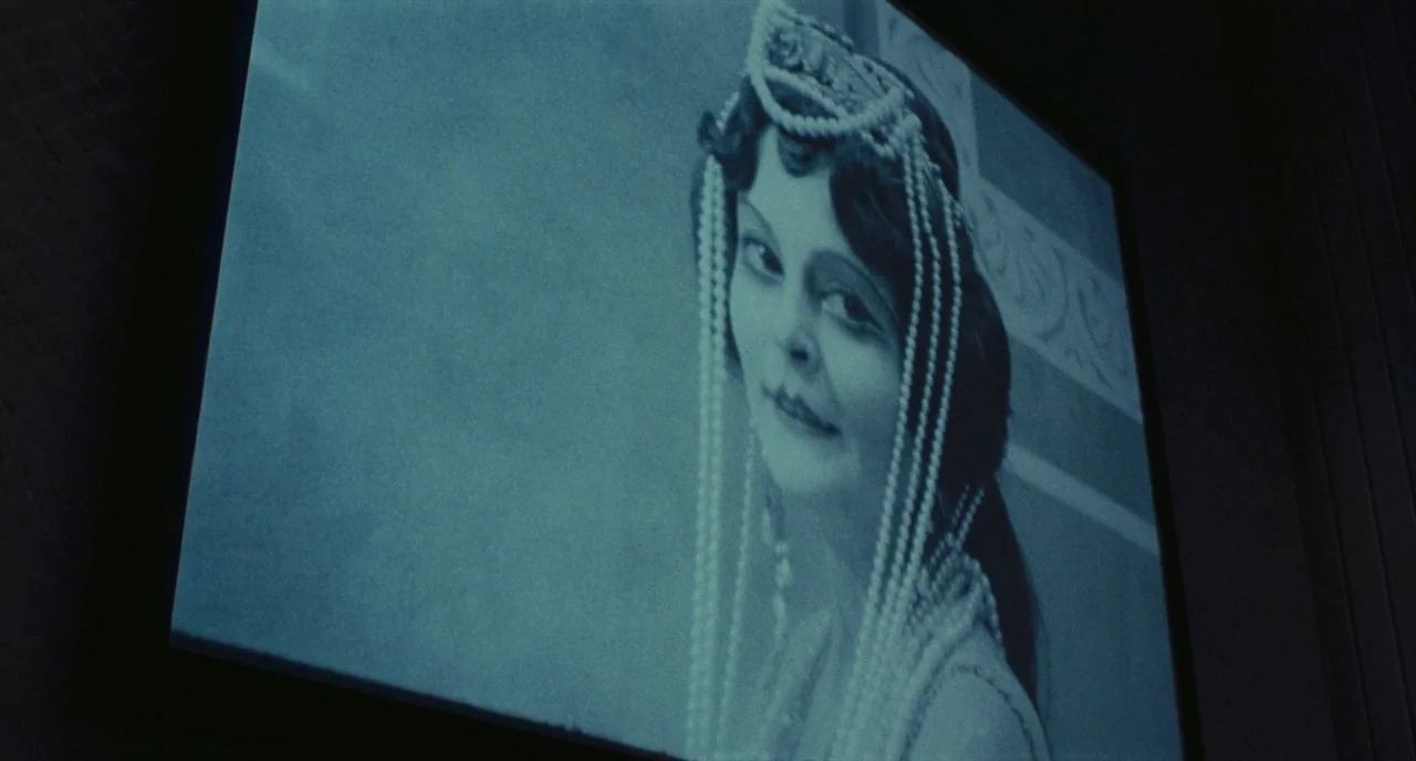 Roma (1972) movie still: closeup — A close-up of a vintage film projection displayed on a screen in darkness. The woman onscreen wears a decorative…