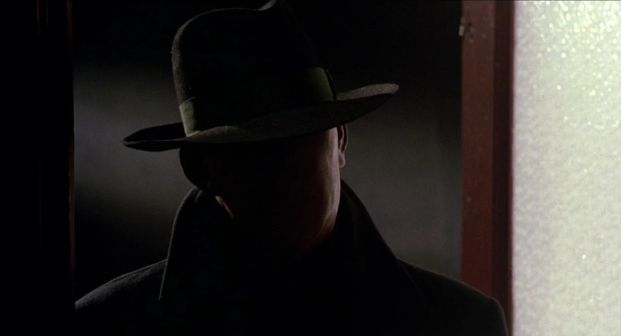 Dick Tracy (1990) movie still: closeup — A dark, high-contrast interior doorway frames the silhouette of a person. The subject stands partially…