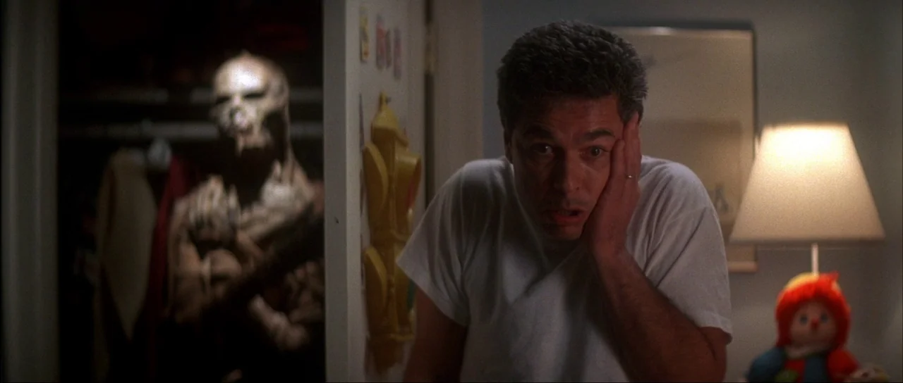 The Monster Squad (1987) movie still: medium — A dimly lit room contains an open closet housing a dark, leathery creature. A man in a white t-shirt…