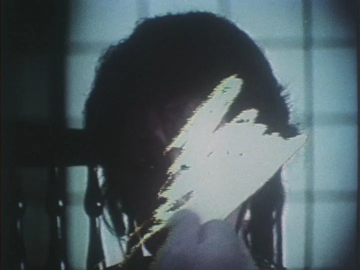 The Eraser (1977) movie still: closeup — A dark indoor space with a window grid visible in the background. A person holds a bright, glowing sheet of…