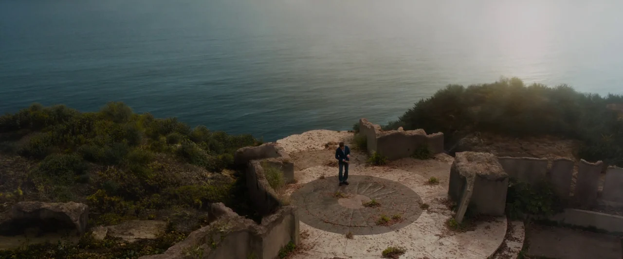 Iron Man 3 (2013) movie still: wide — A stone platform overlooking the ocean is surrounded by weathered concrete walls and vegetation. A lone man…