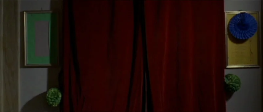 Four Flies On Grey Velvet (1971) movie still: wide — A wall is draped with heavy dark red velvet curtains and decorated with two frames. Two green…