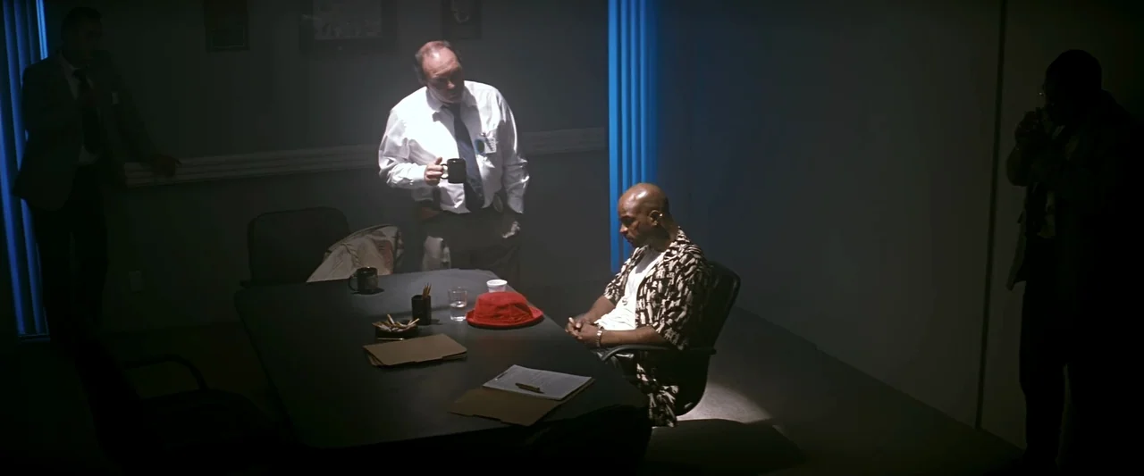 The Last Boy Scout (1991) movie still: wide — A dimly lit room with a conference table and three men present. The man in the patterned shirt sits as…