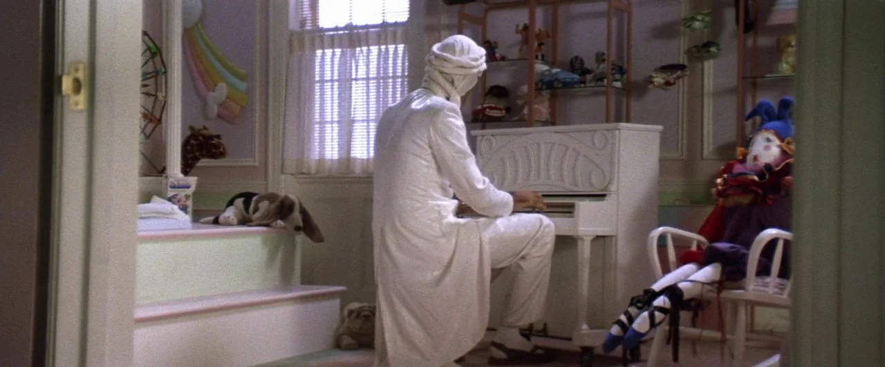 The Witches of Eastwick (1987) movie still: medium — A decorated nursery room contains a toy piano, shelves with toys, and a stuffed jester. A…
