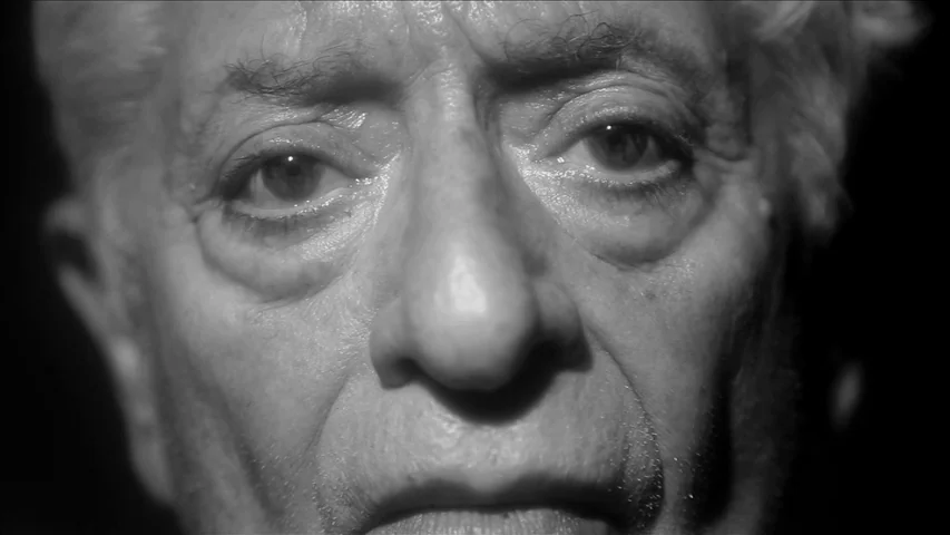 Keyhole (2011) movie still: closeup — A man's face fills the frame against a completely dark, featureless background. The subject maintains eye…