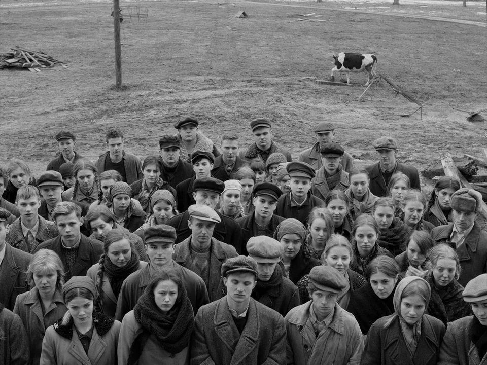 Cold War (2018) movie still: wide — A dense group of people in 1940s attire stand closely together in an open field. A single cow grazes on the…