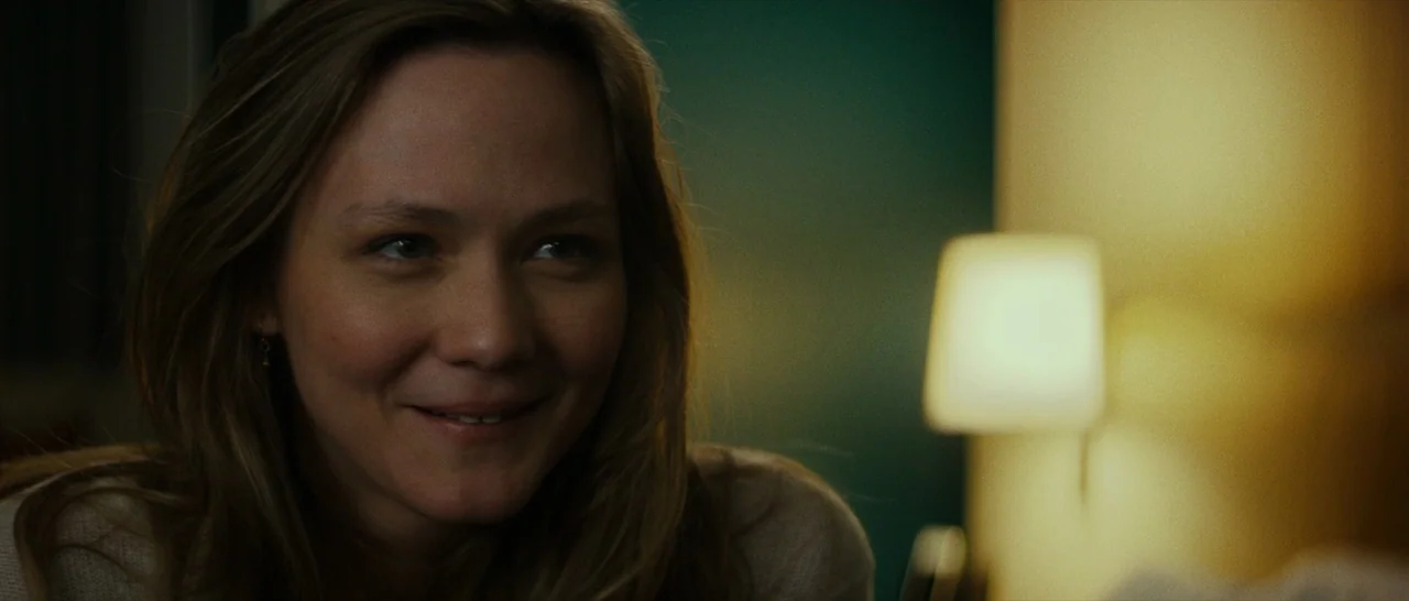 Dog Eat Dog (2016) movie still: closeup — A dimly lit room features a blurred, glowing lamp against a dark teal wall. A woman with shoulder-length…