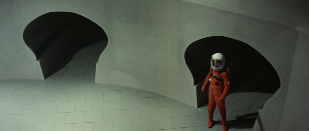 Invasion of Astro Monster (1965) movie still: wide — A minimalist curved hallway features two large, organic-shaped archways cut into a grey wall.…