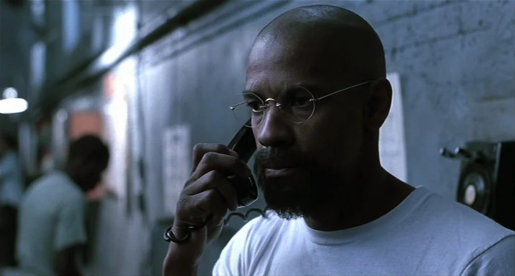 The Hurricane (1999) movie still: closeup — A dimly lit room with blue-tinted concrete walls and an institutional appearance. A bald man wearing…