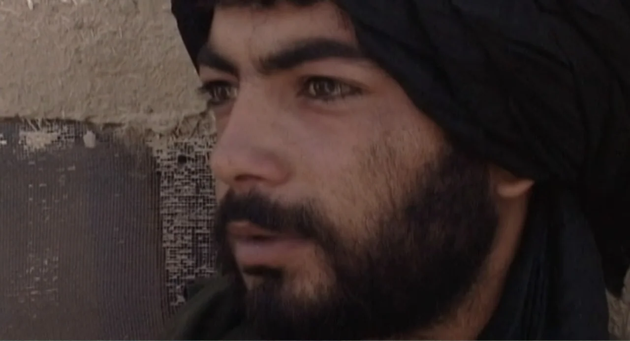 Afghanistan's Opium Trail (2007) movie still: closeup — A close-up of a man positioned against a rough, textured earthen wall. He looks toward the…