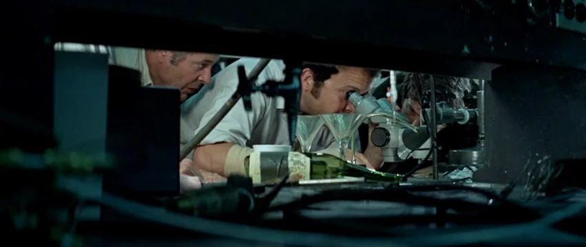 Brewster McCloud (1970) movie still: medium — A cluttered laboratory workbench is filled with glass instruments, cables, and dark equipment. Two…