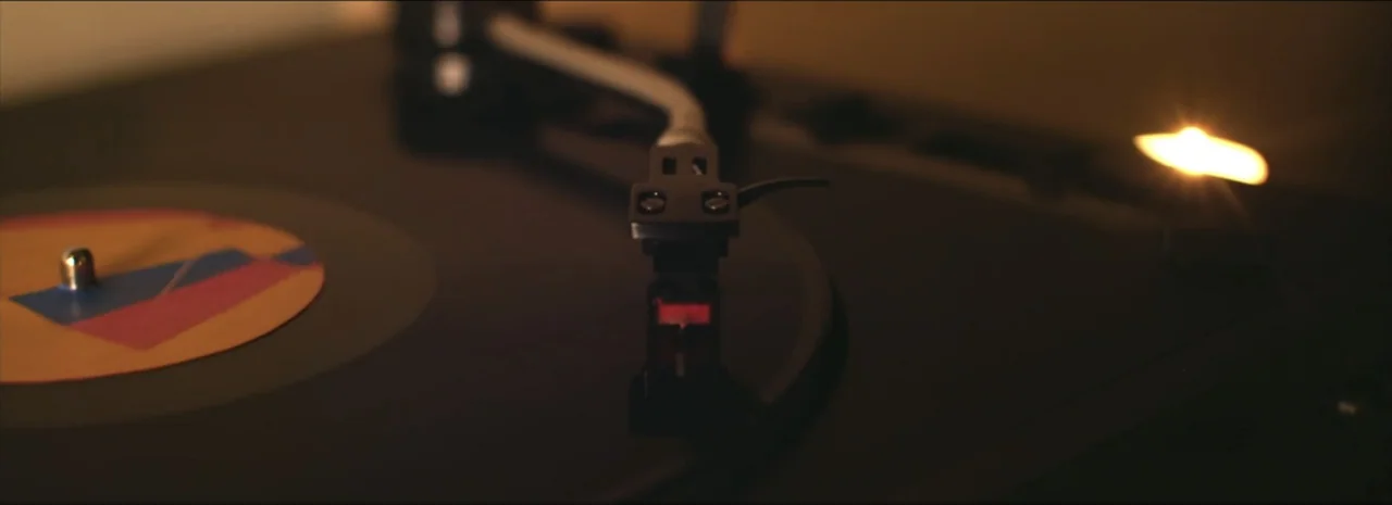 DannyBoy (2020) movie still: closeup — A close-up view shows a black turntable with a spinning colorful vinyl record. The needle sits precisely in…