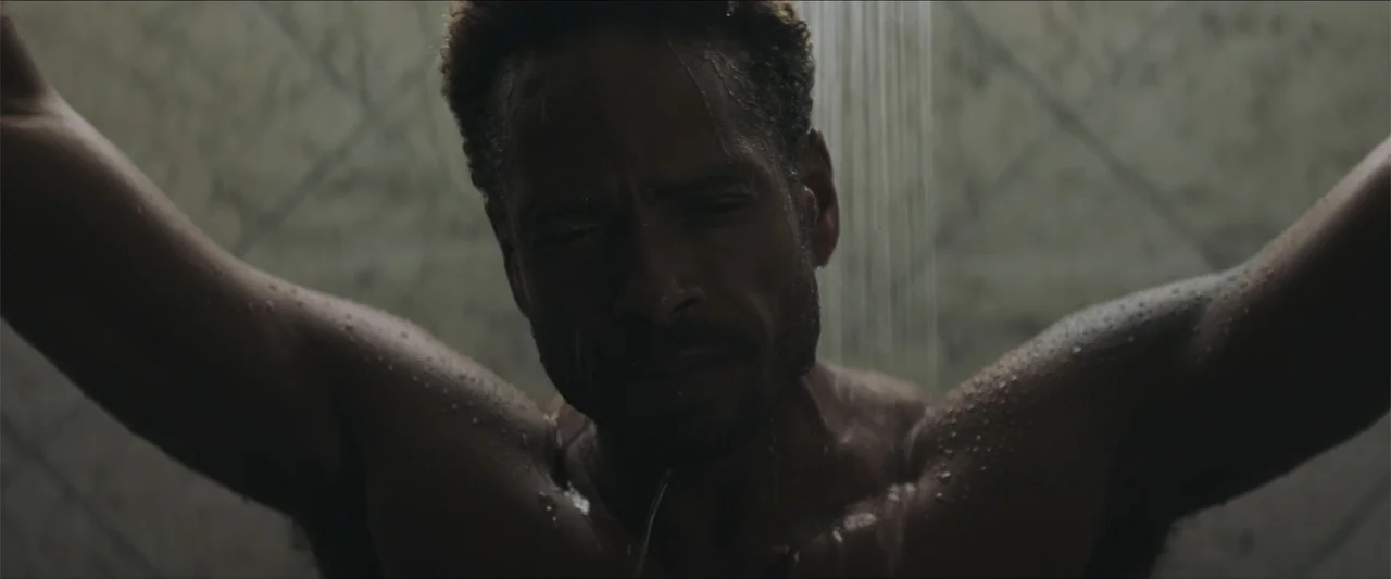 Redemption Day (2021) movie still: closeup — A tiled walk-in shower stall with dim overhead lighting and water streaming down. A shirtless man…