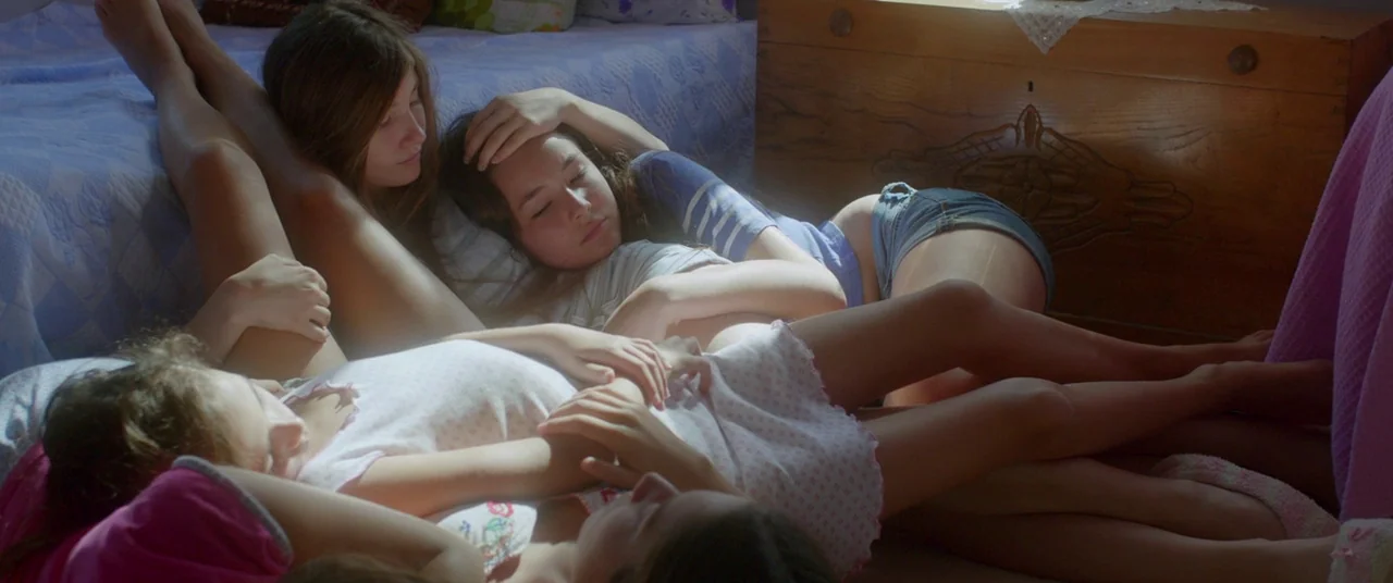 Mustang (2015) movie still: medium — Three teenage girls rest together on a floor covered in blankets and pillows. Sunlight streams across them from…