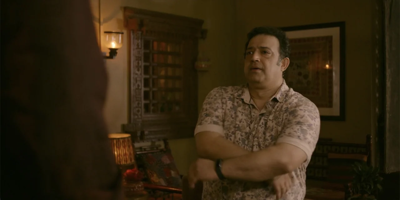 Maja Stoneface (1996) movie still: medium — A dimly lit room features a wooden wall carving and a framed picture. A middle-aged man stands in the…