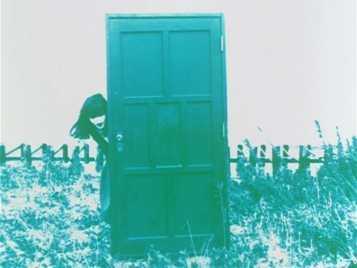 Labyrinth Tale (1975) movie still: medium — A freestanding wooden door is positioned vertically within an open, grassy outdoor landscape. A person…