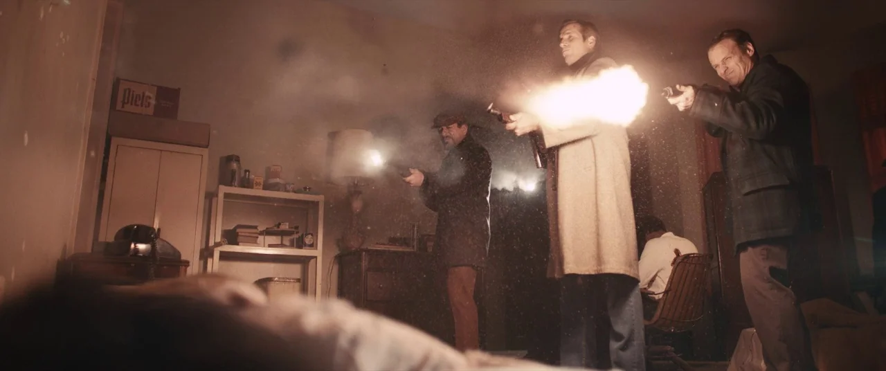 Judas and the Black Messiah (2021) movie still: wide — An interior space contains a shelf, a lamp, and several men firing weapons. Gunpowder smoke…