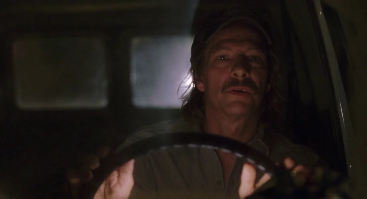 Adaptation (2002) movie still: medium — The inside of a dark vehicle at night with rectangular windows in the rear. A man grips the steering wheel…