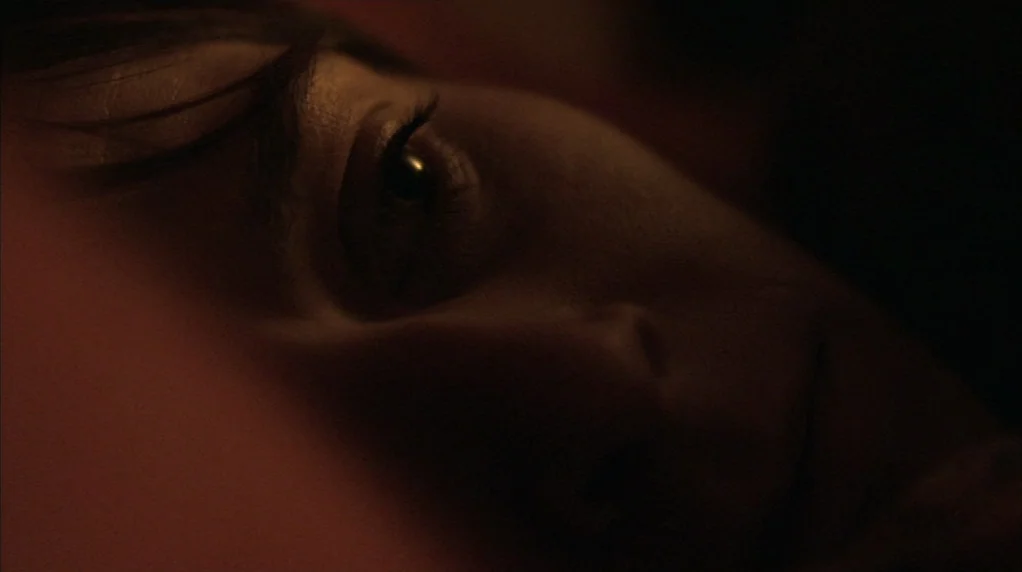 Red Road (2006) movie still: closeup — A person lies in a dark, dimly lit space, likely a bed. The camera is positioned very close to the subject's…