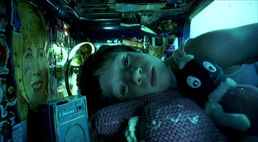Hedwig and the Angry Inch (2001) movie still: closeup — A cramped bunk bed interior is lined with stickers and cluttered with small objects. A young…