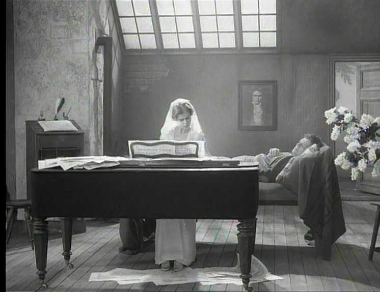 In The Presence of a Clown (1997) movie still: wide — An attic room features a large slanted window, musical scores scattered on the floor, and a…