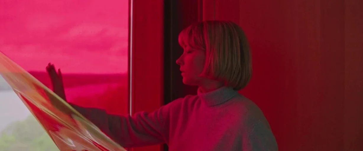 Swallow (2020) movie still: medium — A woman stands in a dim room next to a window covered by plastic. She touches the surface of the pink material…