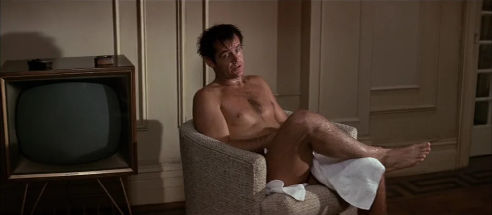 Carnal Knowledge (1971) movie still: medium — A hotel room with wood paneled walls and a vintage television set on a stand. A man sits in a chair…