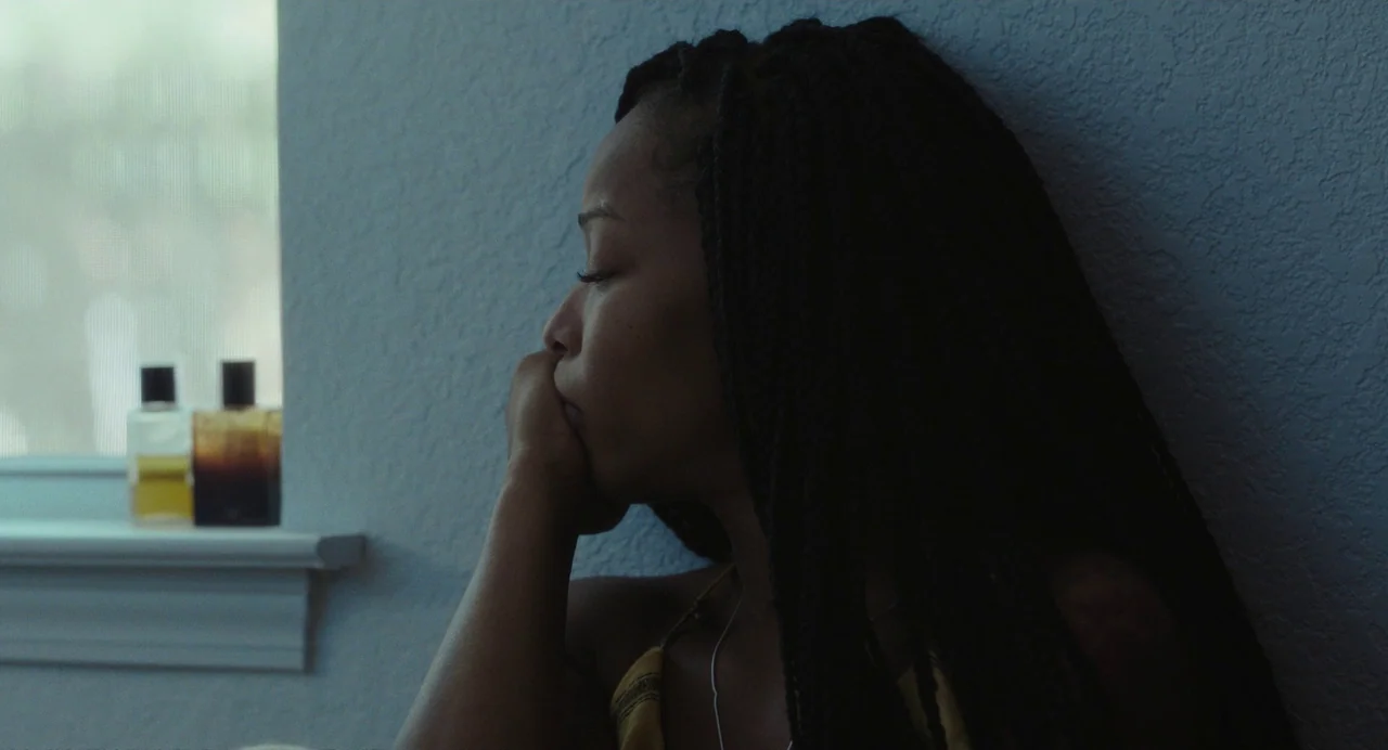Test Pattern (2019) movie still: medium — A dimly lit room with textured blue walls features a small window sill. The subject leans against the wall…