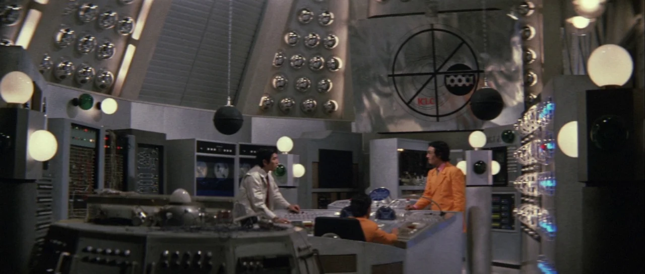 Godzilla Vs Gigan (1972) movie still: wide — A futuristic 1970s control room features silver walls covered with small round light fixtures. Three…