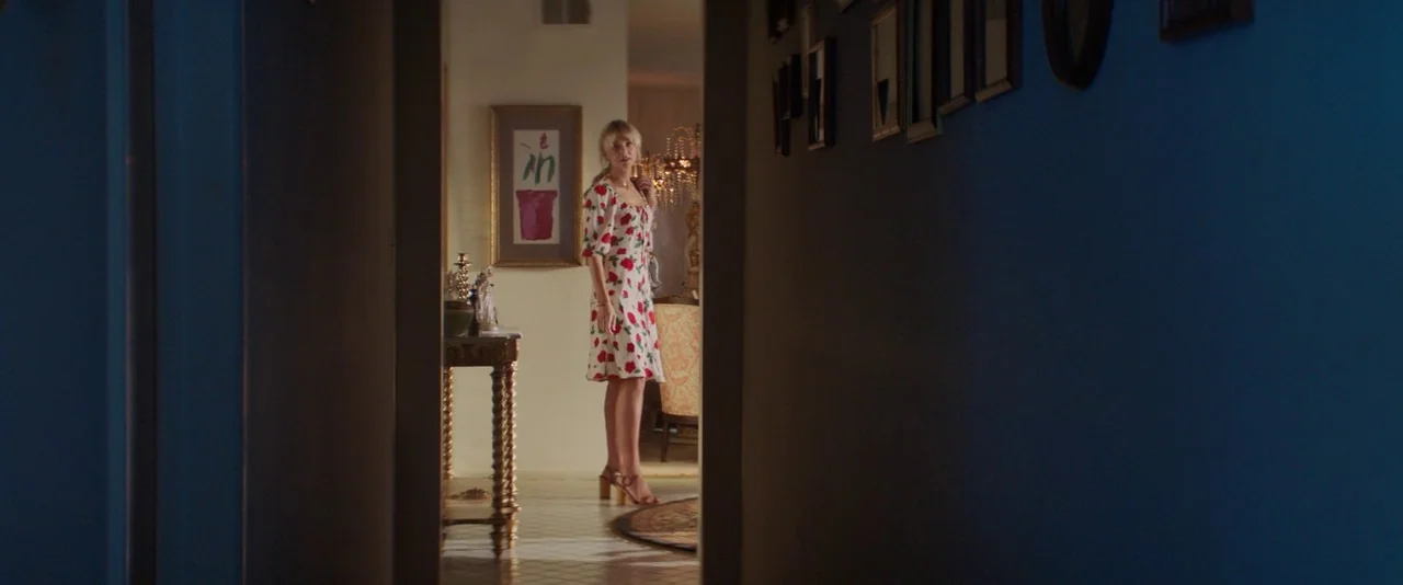 Promising Young Woman (2020) movie still: fullbody — A woman in a floral dress stands in a brightly lit room viewed through a dark hallway. The…