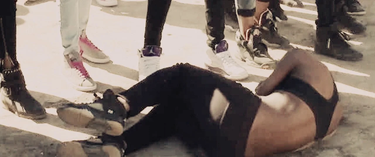 Girlhood (2014) movie still: medium — A person lies curled on a painted white crosswalk surrounded by several standing people. The surrounding legs…