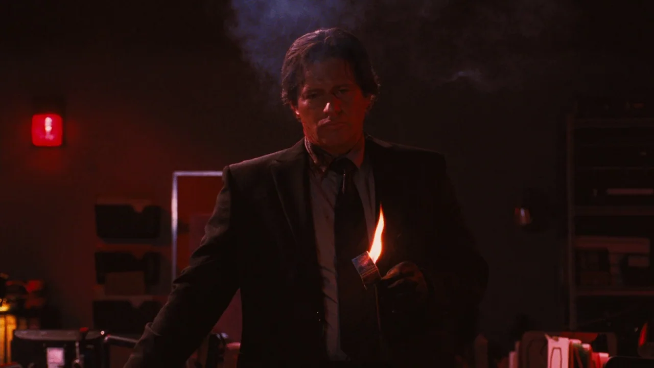Saw VI movie still: medium — A dimly lit room bathed in red light with indistinct shelves and office equipment. A man in a suit stands in the center…