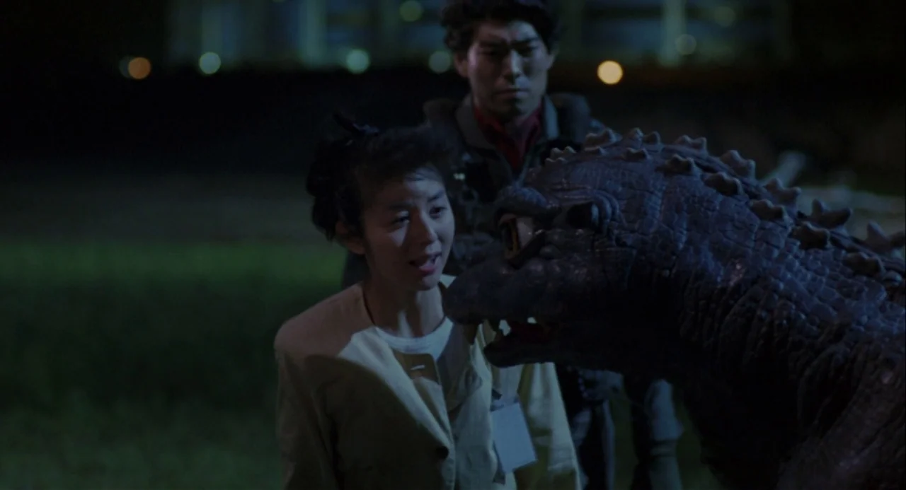 Godzilla vs. Mechagodzilla II (1993) movie still: medium — A dark grassy area at night with indistinct city lights in the distance. A woman gazes at…