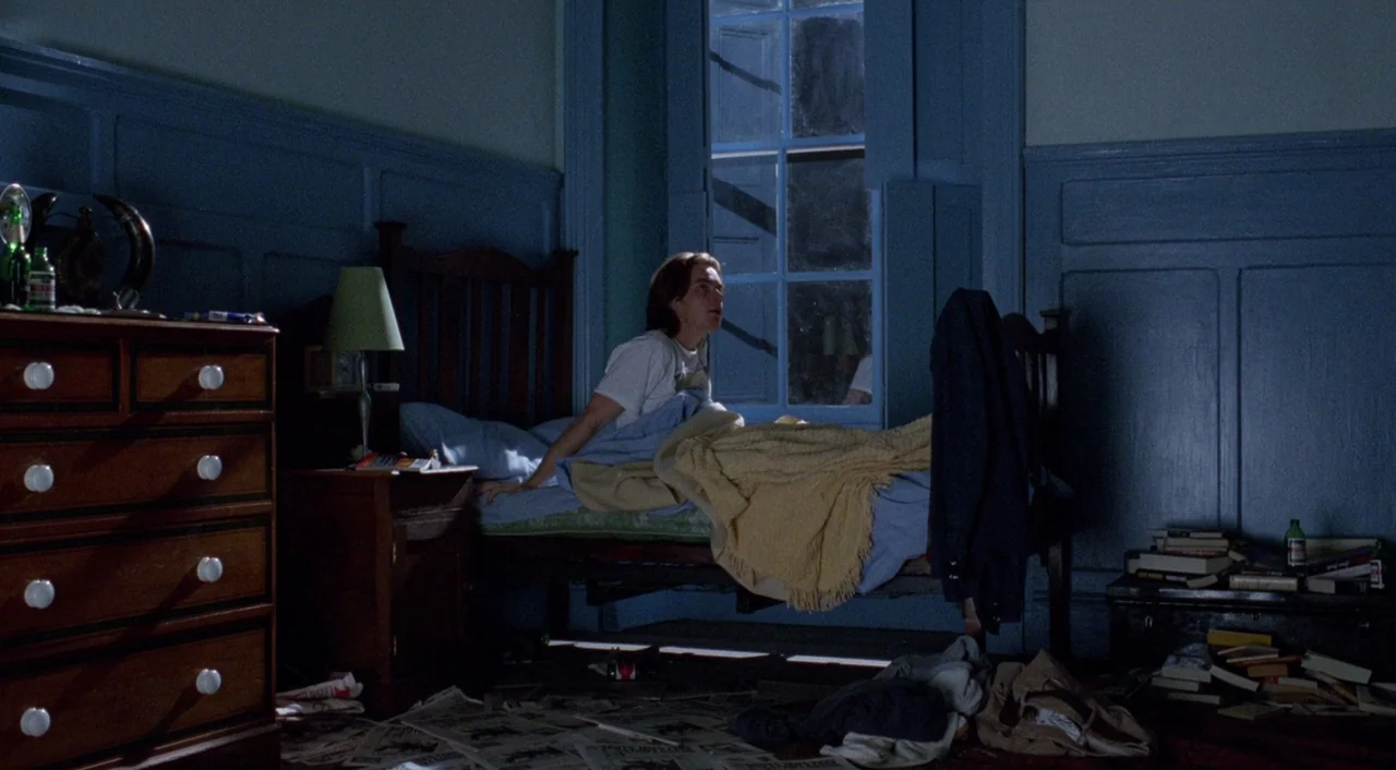 Shallow Grave (1994) movie still: wide — A dark bedroom features blue wainscoting and clutter scattered across the floor. A young man sits up in bed…