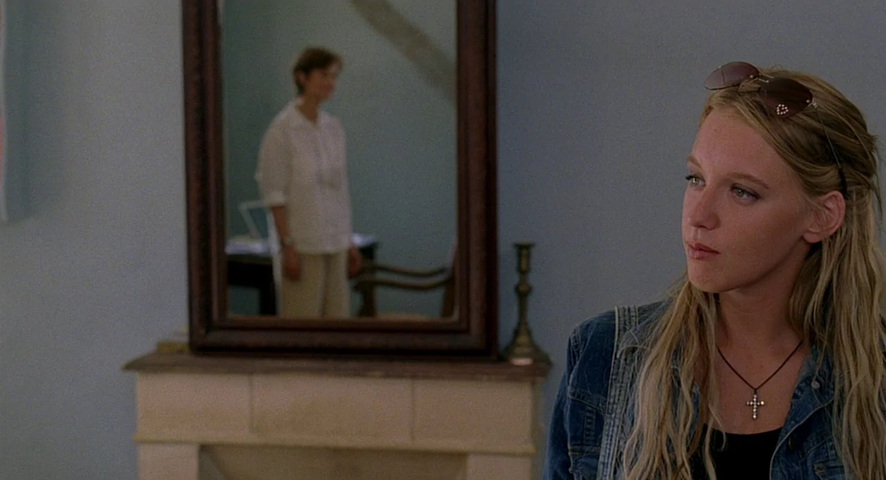 Swimming Pool (2003) movie still: medium — A light blue room features a framed mirror hanging on a wall above a mantle. A young woman in the…