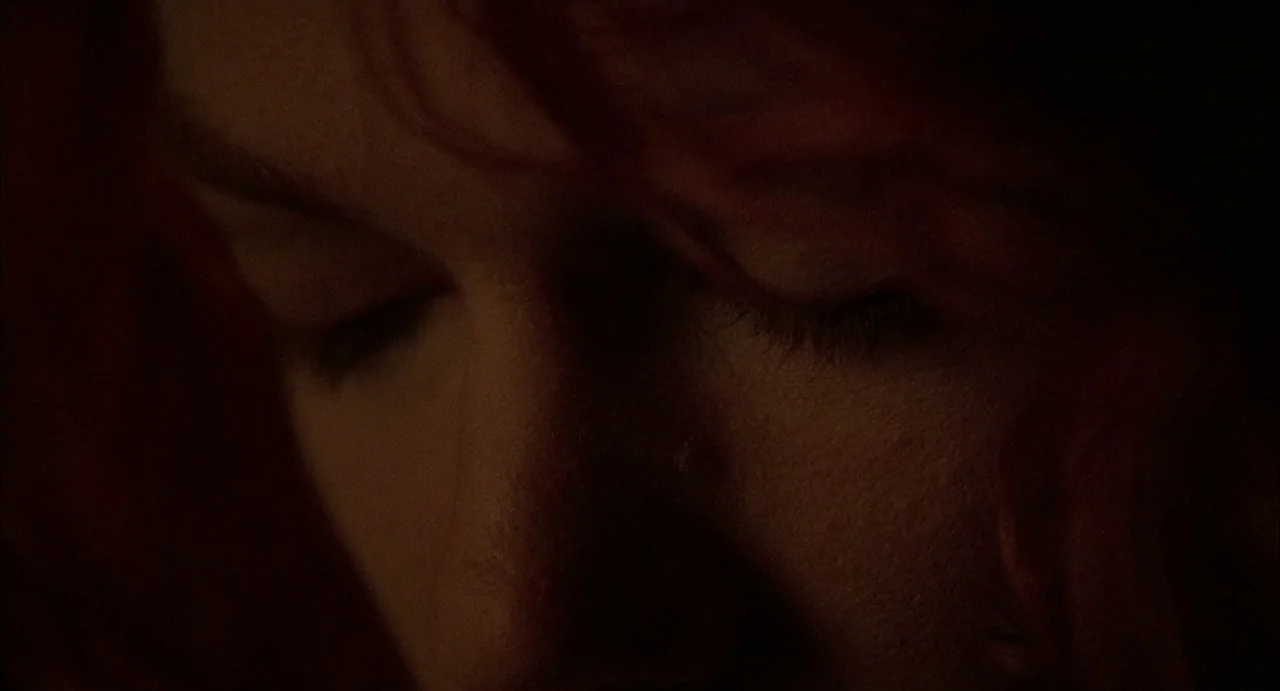 Hardware (1990) movie still: closeup — A close-up of a person's face set in an dimly lit environment. The subject has their eyes closed and hair…
