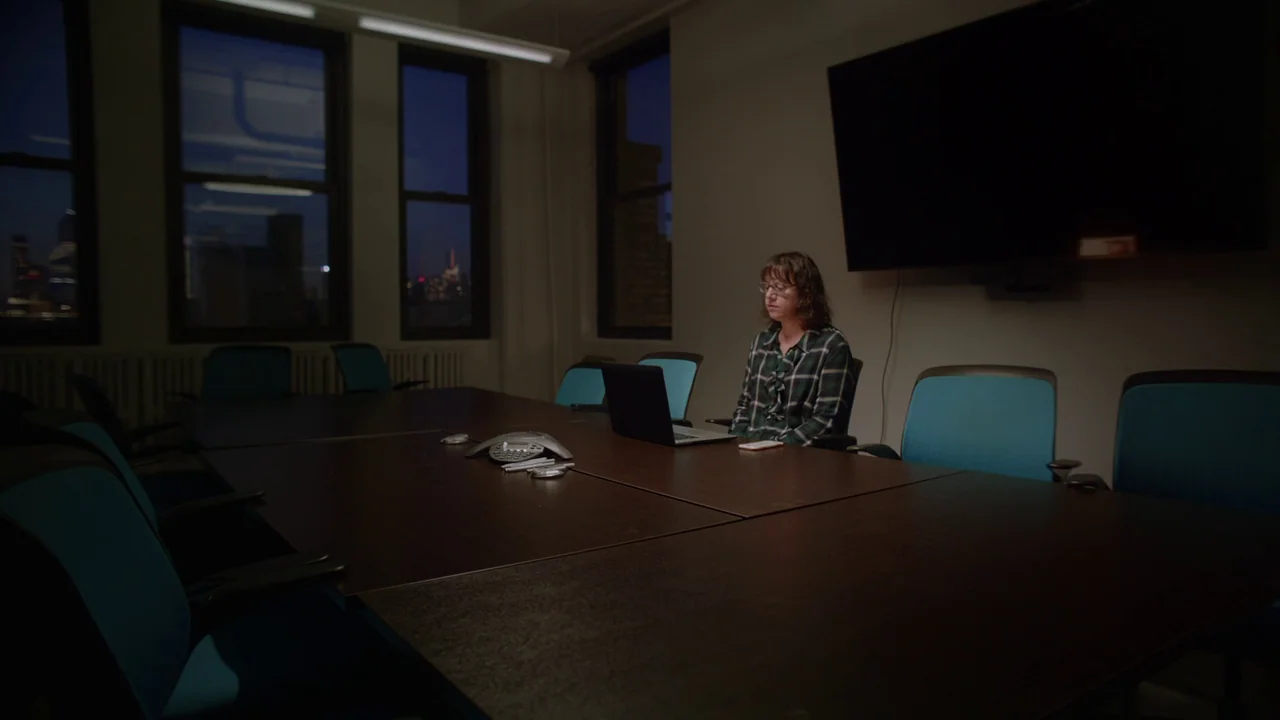 The Feeling That the Time for Doing Something Has Passed (2023) movie still: wide — A dark corporate conference room with a large mahogany table and…