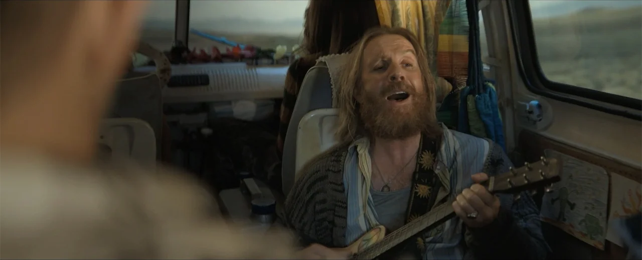 Venom: The Last Dance (2024) movie still: medium — The interior of a camper van with a passenger facing the driver. A man with a full beard plays a…