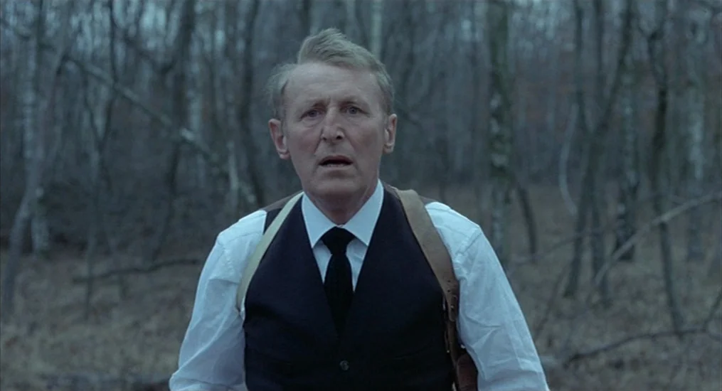 Le Cercle Rouge (1970) movie still: medium — A dense patch of leafless birch trees provides a muted background during an overcast day. An older man…