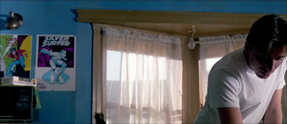 Reservoir Dogs (1992) movie still: medium — A room with bright blue walls featuring comic book posters on the side wall. A man in a white t-shirt…