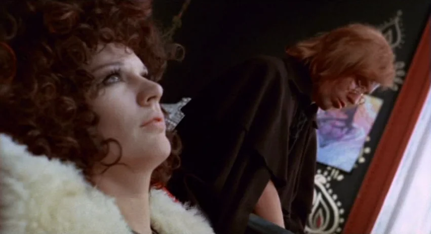 A Lizard In A Woman’s Skin (1971) movie still: medium — A room interior features a decorative black panel with ornamental designs behind the…